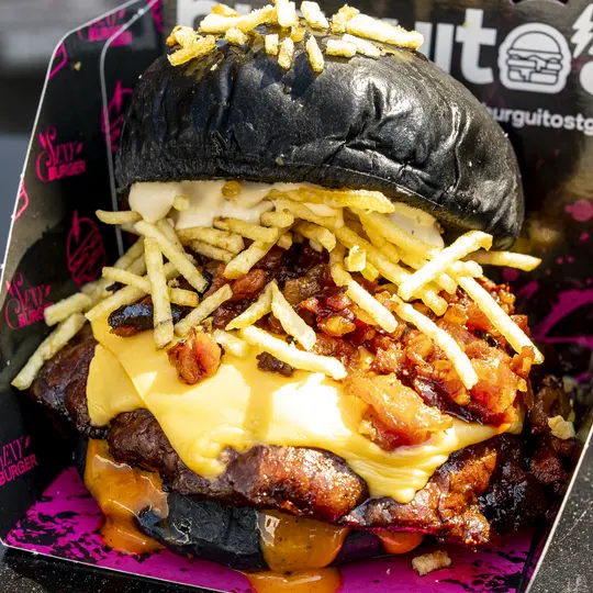 Burger sobre pan brioche negro, con queso fundido y patatas paja